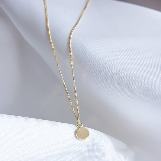 Gouden hanger in de vorm van een muntje waar een letter in gestempeld kan worden.